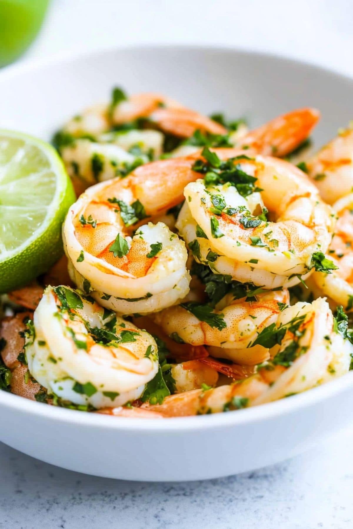 Shrimp with cilantro and lime juice garnished with lime sliced in half served in a white bowl.