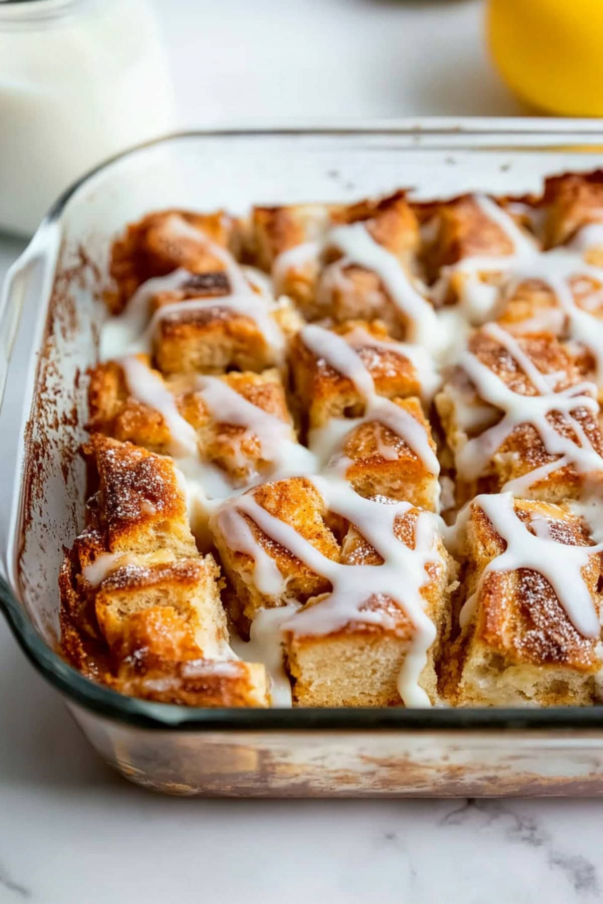 Cinnamon roll in a baking dish with white glaze on top.