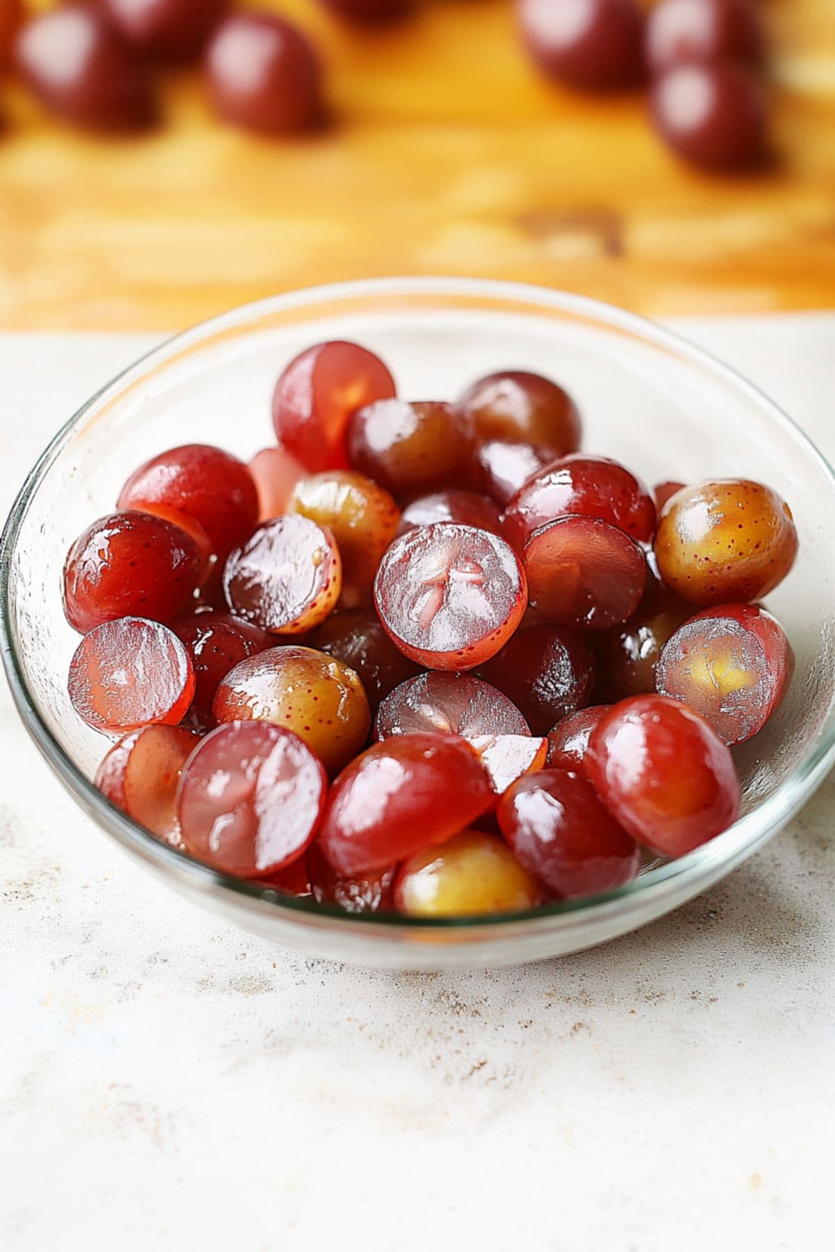 Sliced in half red grapes in a small glass bowl.