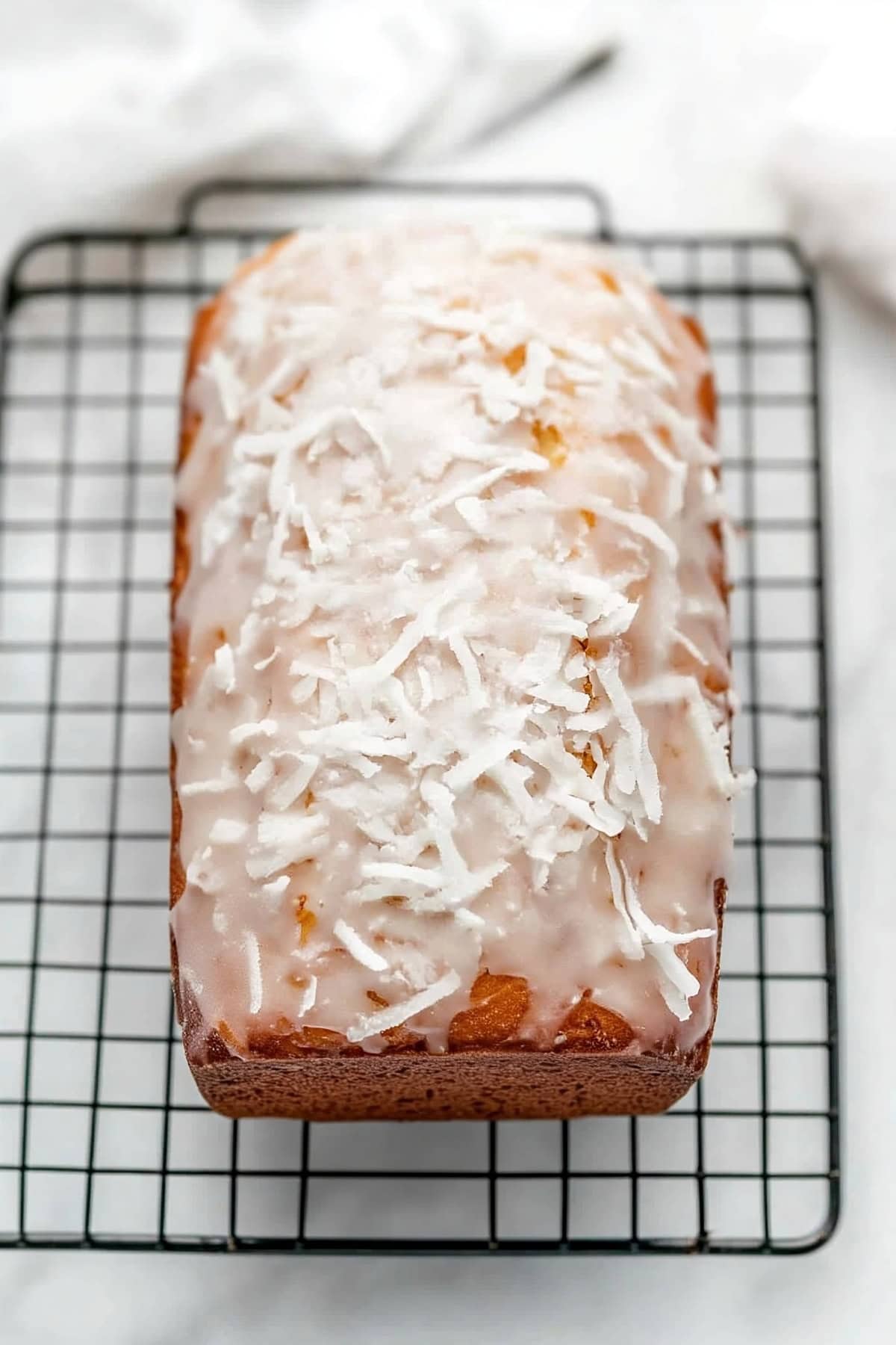 Overhead view of a freshly baked loaf of coconut bread topped with shiny glaze and coconut flakes.