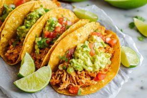 Cheesy and crispy chicken tacos with guacamole, salsa and lime on parchment paper.