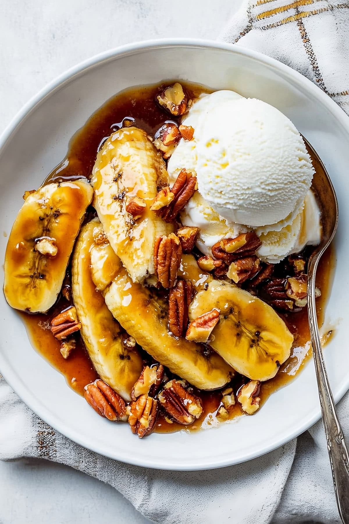 Bananas foster with chopped pecans and ice cream in a bowl, top view.