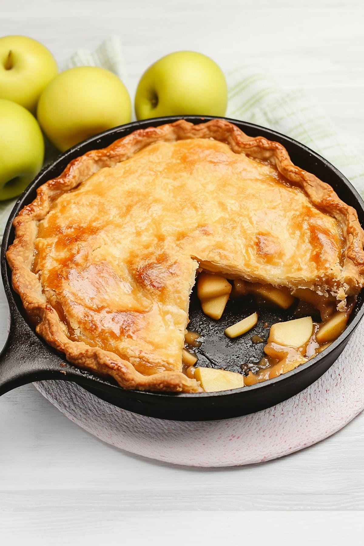 Homemade iron skillet apple pie with a slice removed on a white table