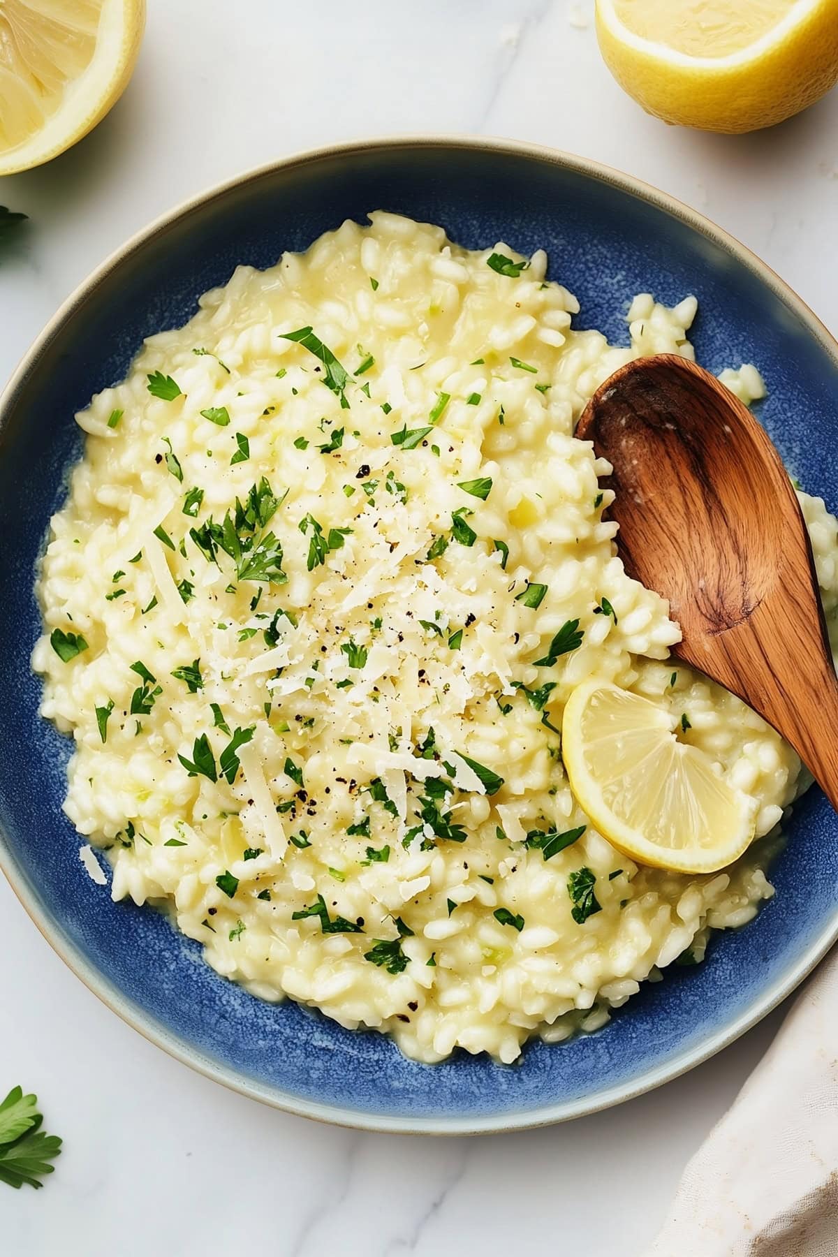 Lemon risotto with grated parmesan and chopped parsley in a blue bowl with a wooden spoon, top view