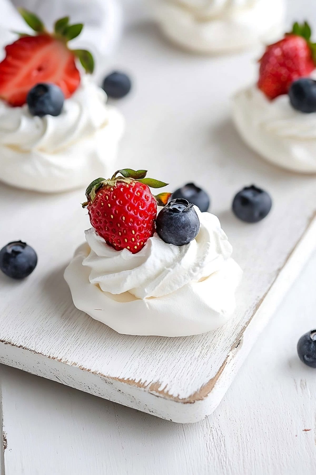 A beautifully presented mini pavlova with whipped cream and a variety of fresh berries, perfect for a summer dessert.