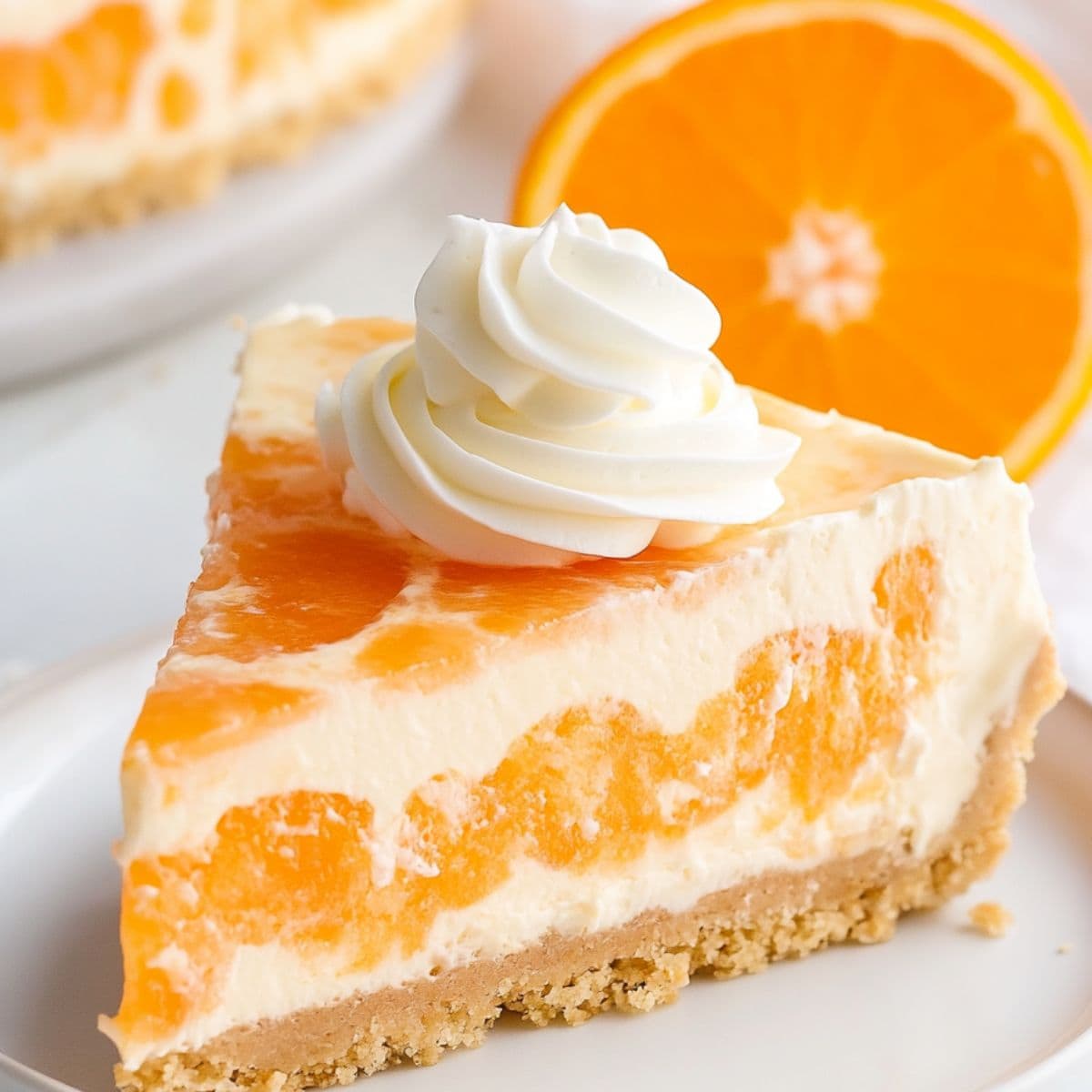 Slice of orange creamsicle cheesecake garnished with whipped cream and orange served on a white plate.