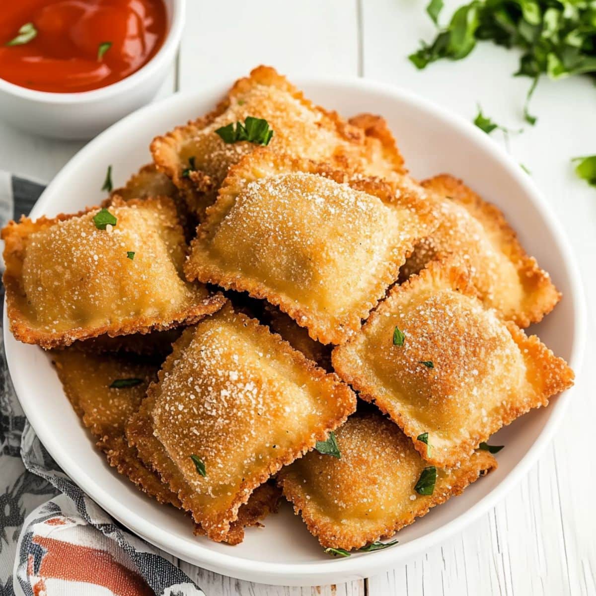 Toasted ravioli served in a white bow with marinara in a dish on the side.