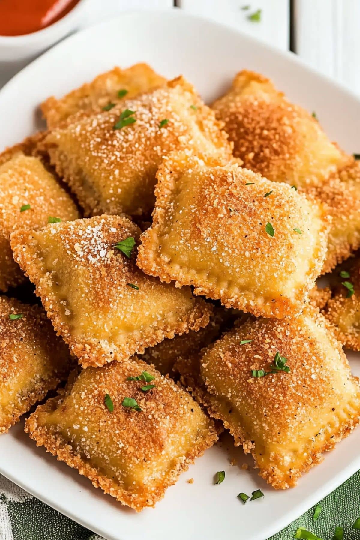 Bunch of breaded and fried toasted ravioli in a plate with marinara sauce on the side.