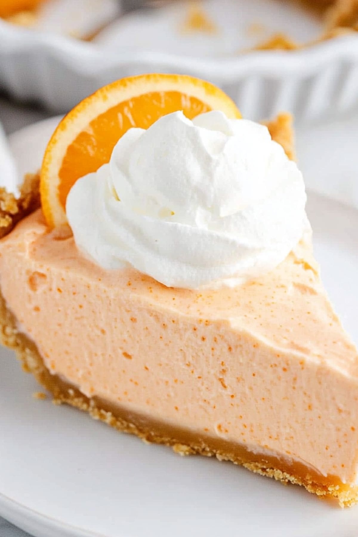 Orange creamsicle pie with whipped cream and orange slice served on a white plate.