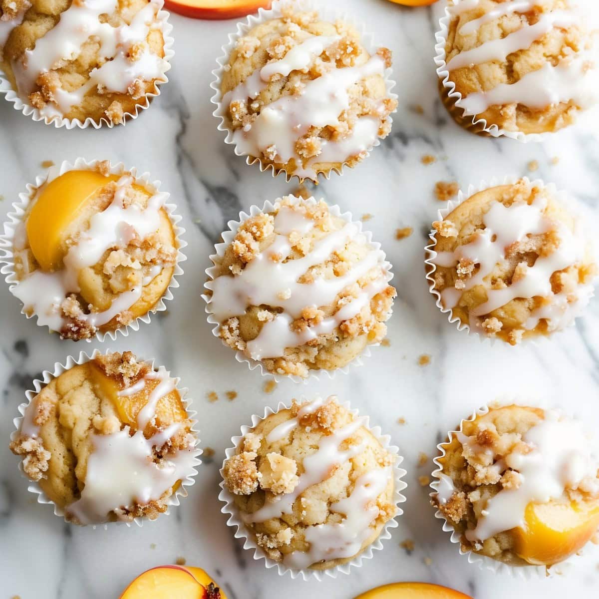 Peach crumble muffins with glaze on a white marble table.