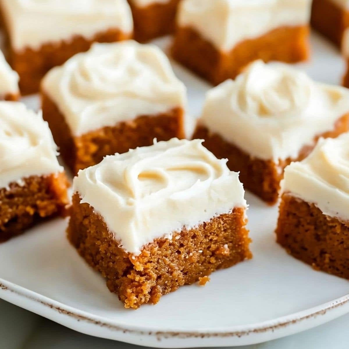 Pumpkin bars with cream cheese frosting arranged on a white plate.