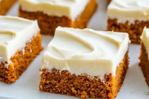 Pumpkin bars with cream cheese frosting arranged on a white marble surface.