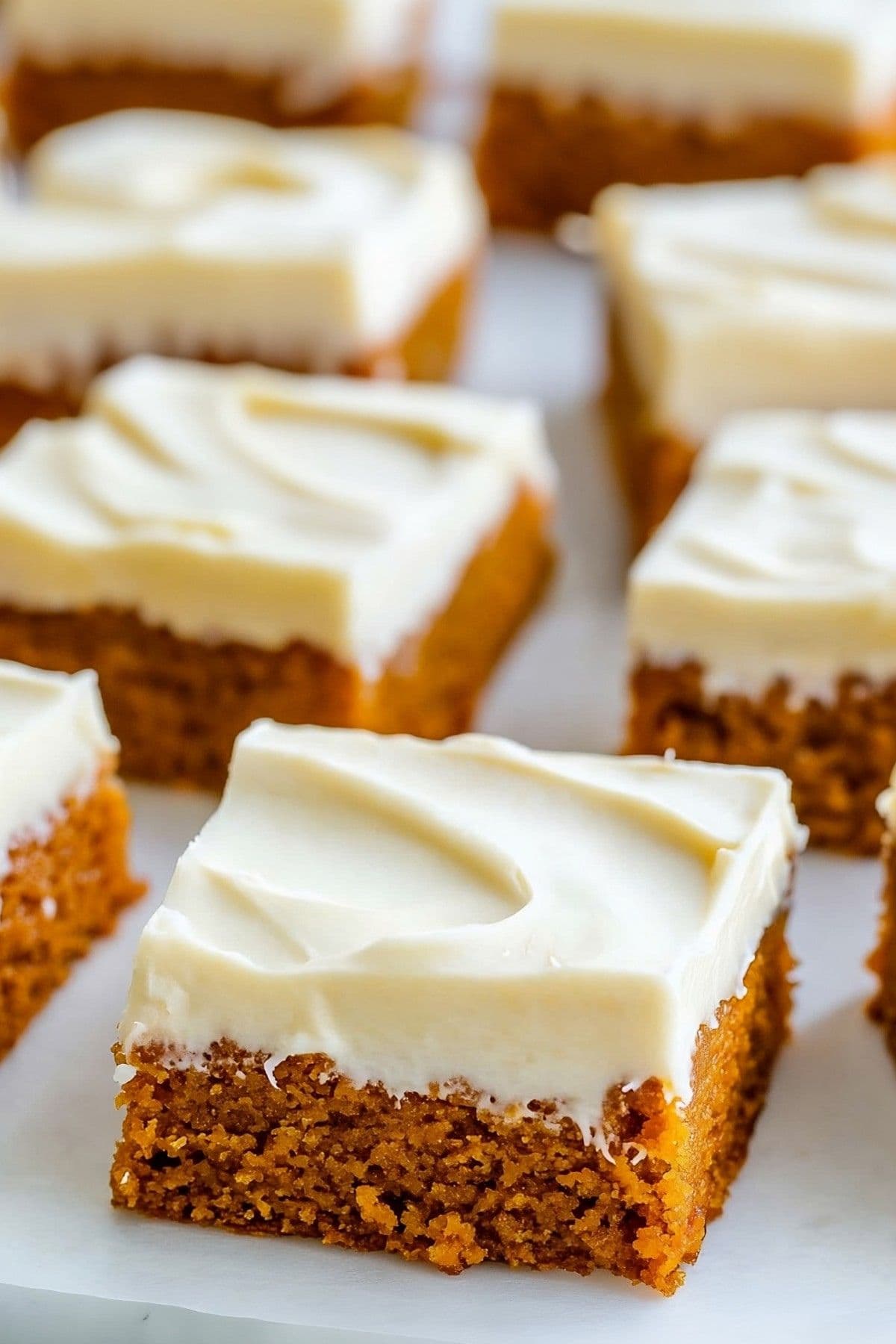 Square slices of pumpkin bars with cream cheese frosting on a white plate.