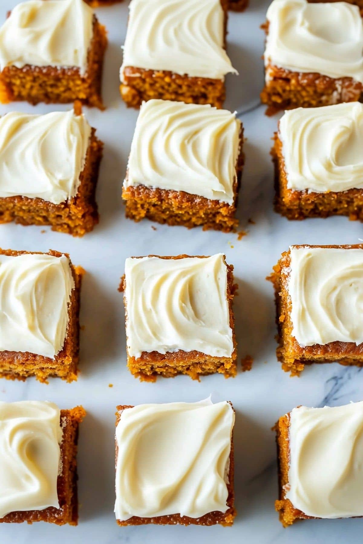 Pumpkin bars with cream cheese frosting sliced on a white marble table, top view