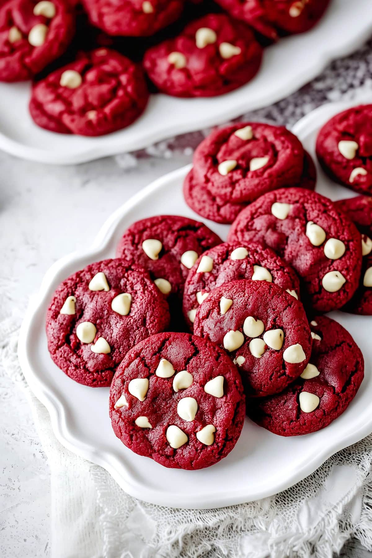 A plate stacked with vibrant red velvet cookies, each studded with creamy white chocolate chips.