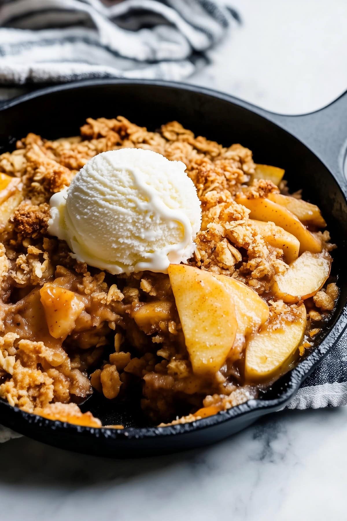 A cast-iron skillet filled with golden-brown apple crisp, topped with a scoop of vanilla ice cream.