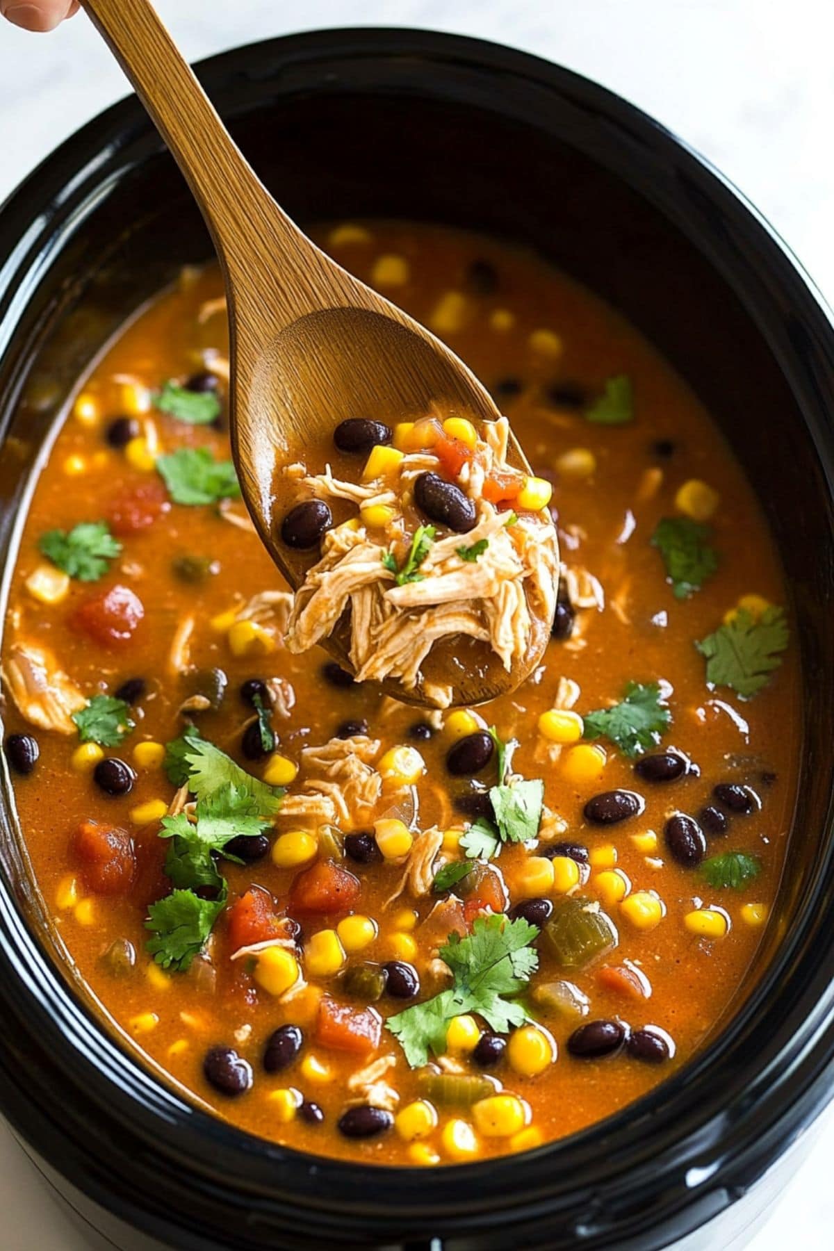 Chicken enchilada soup  inside a slow cooker lifted with a wooden ladle.