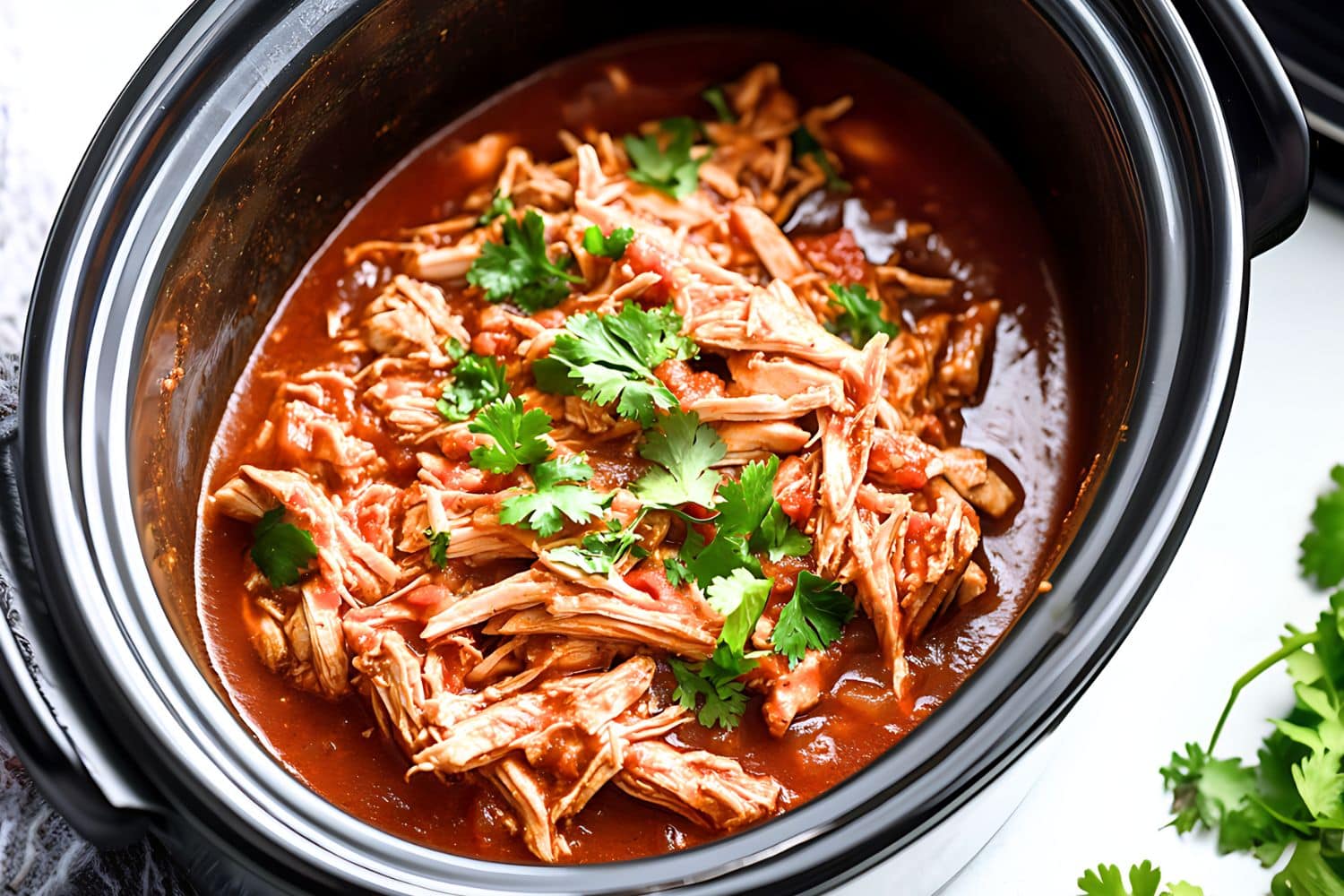 Shredded chicken cooked inside a slow cooker with tomato sauce.