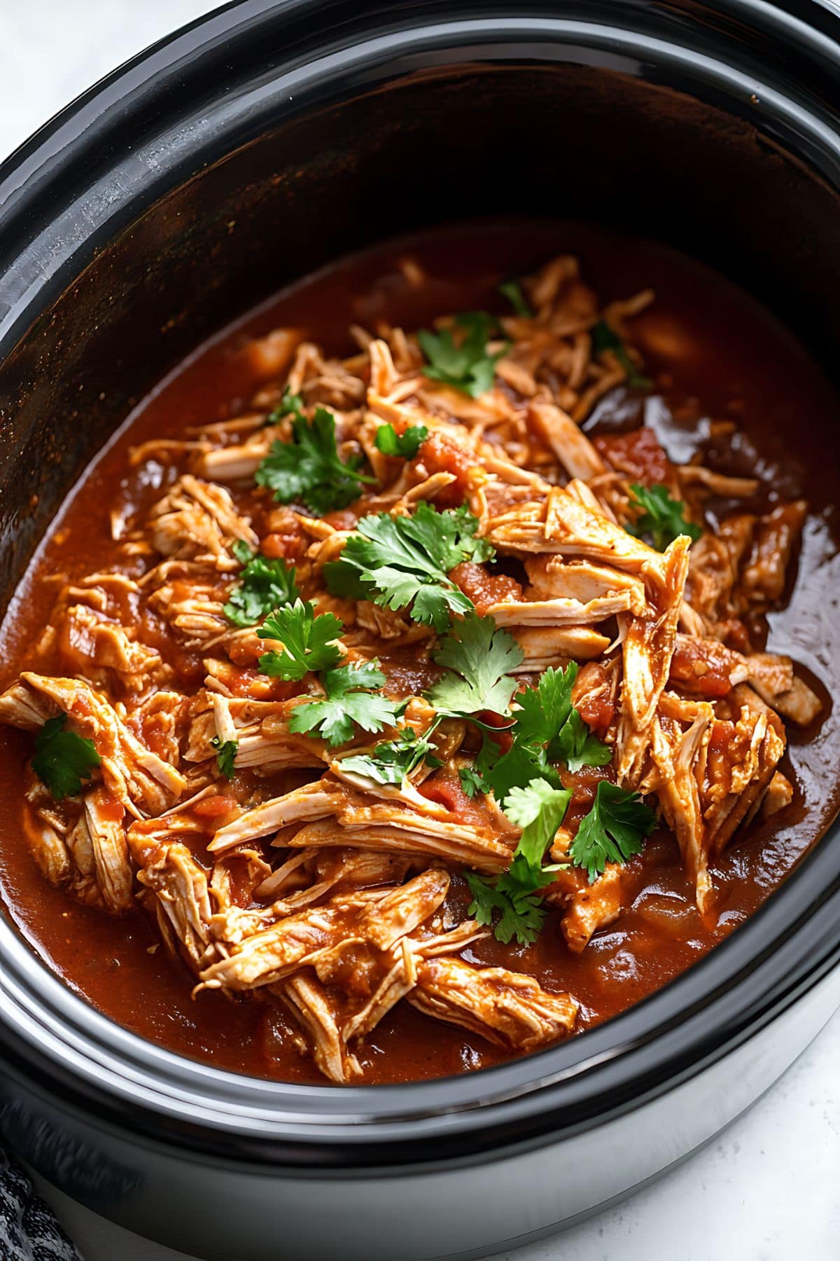 Shredded chicken with tomato based sauce in a slow cooker.