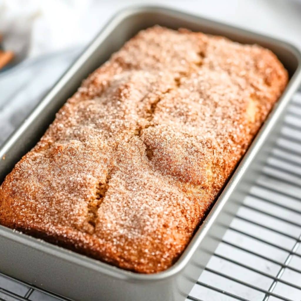 Snickerdoodle bread in a loaf pan sitting on a cooling rack.