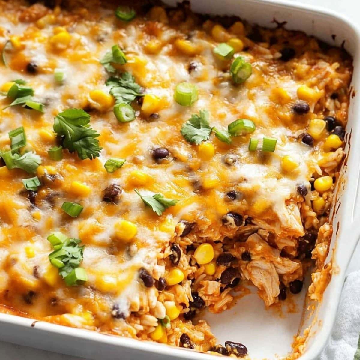 Chicken casserole with melted cheese, rice, chicken chunks, black beans and corn in a rectangular baking dish.