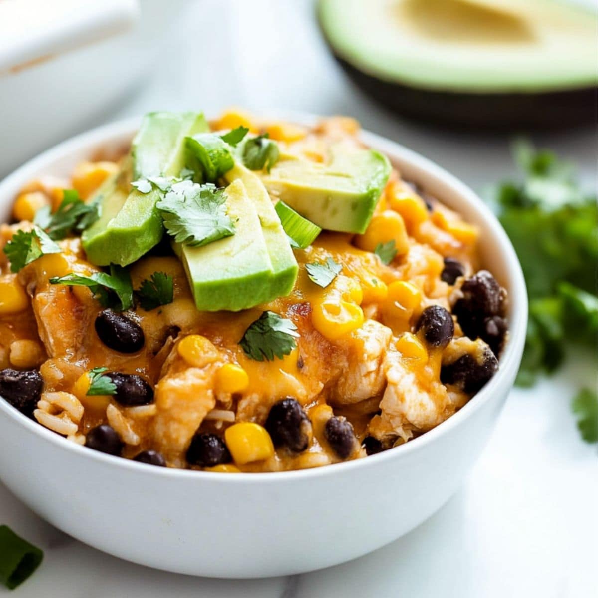 Serving of cheesy chicken casserole in a white bowl garnish with slices of avocado. 