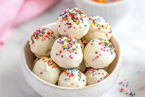 Bunch of sugar cookie truffles in a white bowl with candy sprinkles.