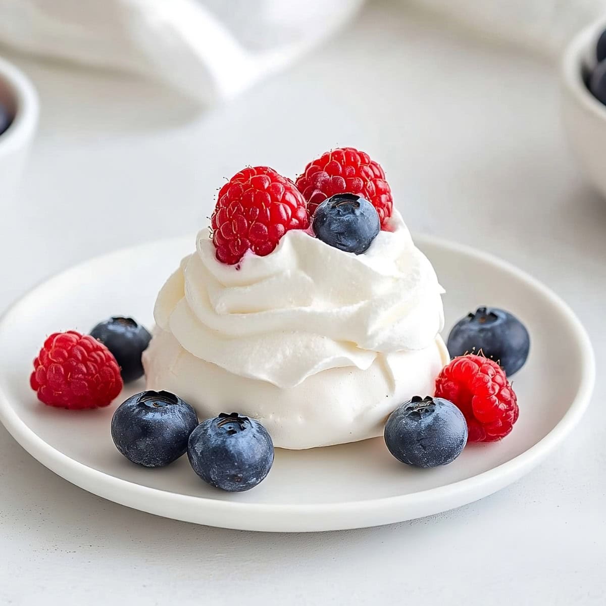 A mini pavlova on a plate with raspberries and blueberries