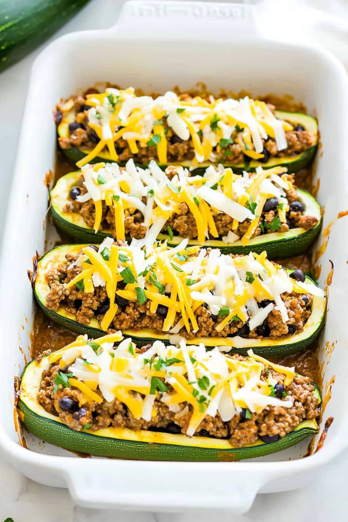 Taco zucchini topped with shredded cheese in a rectangular white baking dish.