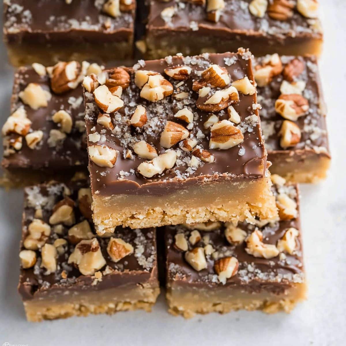 Square slices of toffee bars with chopped pecans, stacked on a light table, top view