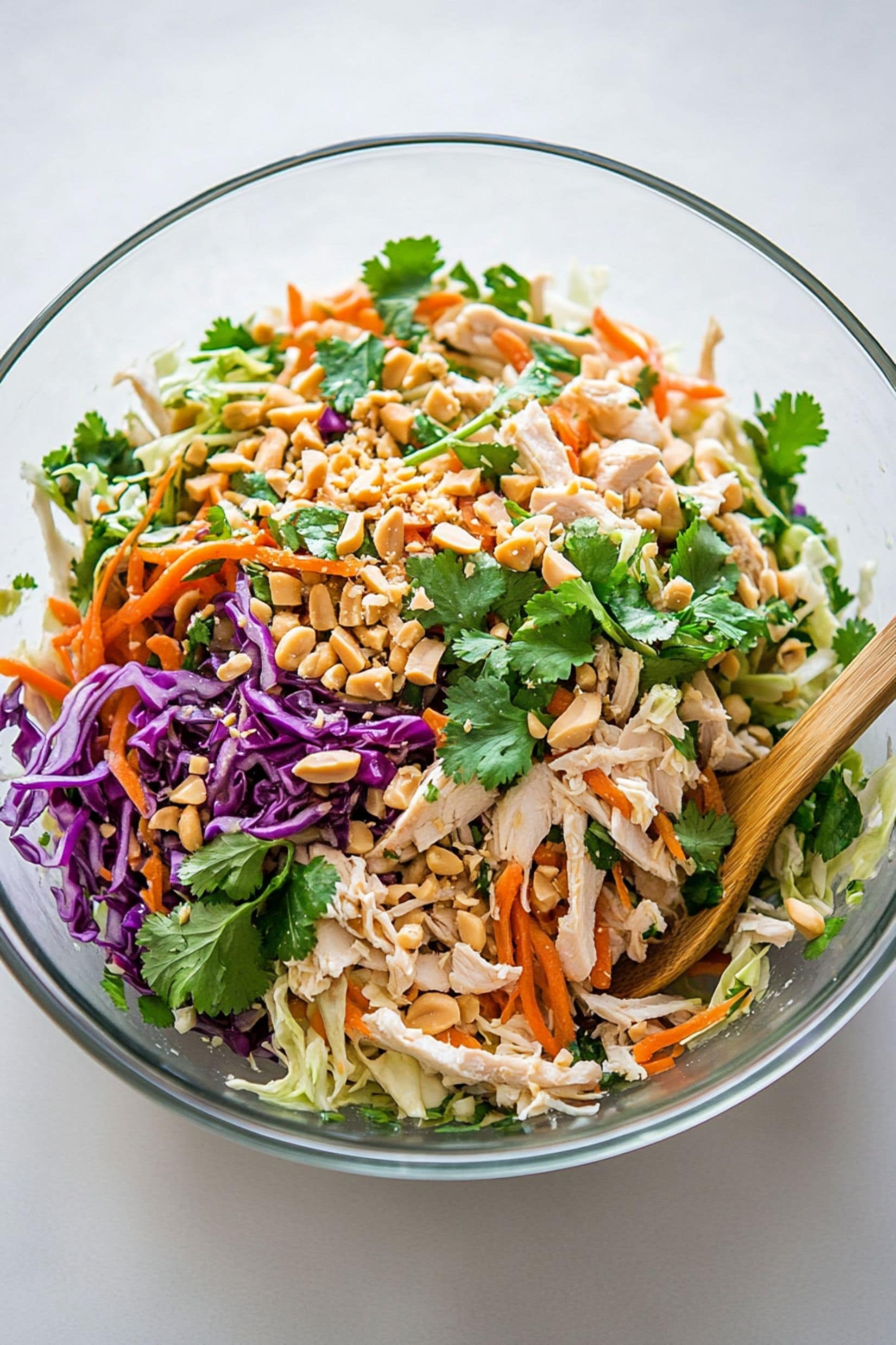 Shredded cabbage, carrots, onions, cilantro leaves and chopped peanuts  in a large glass mixing bowl.