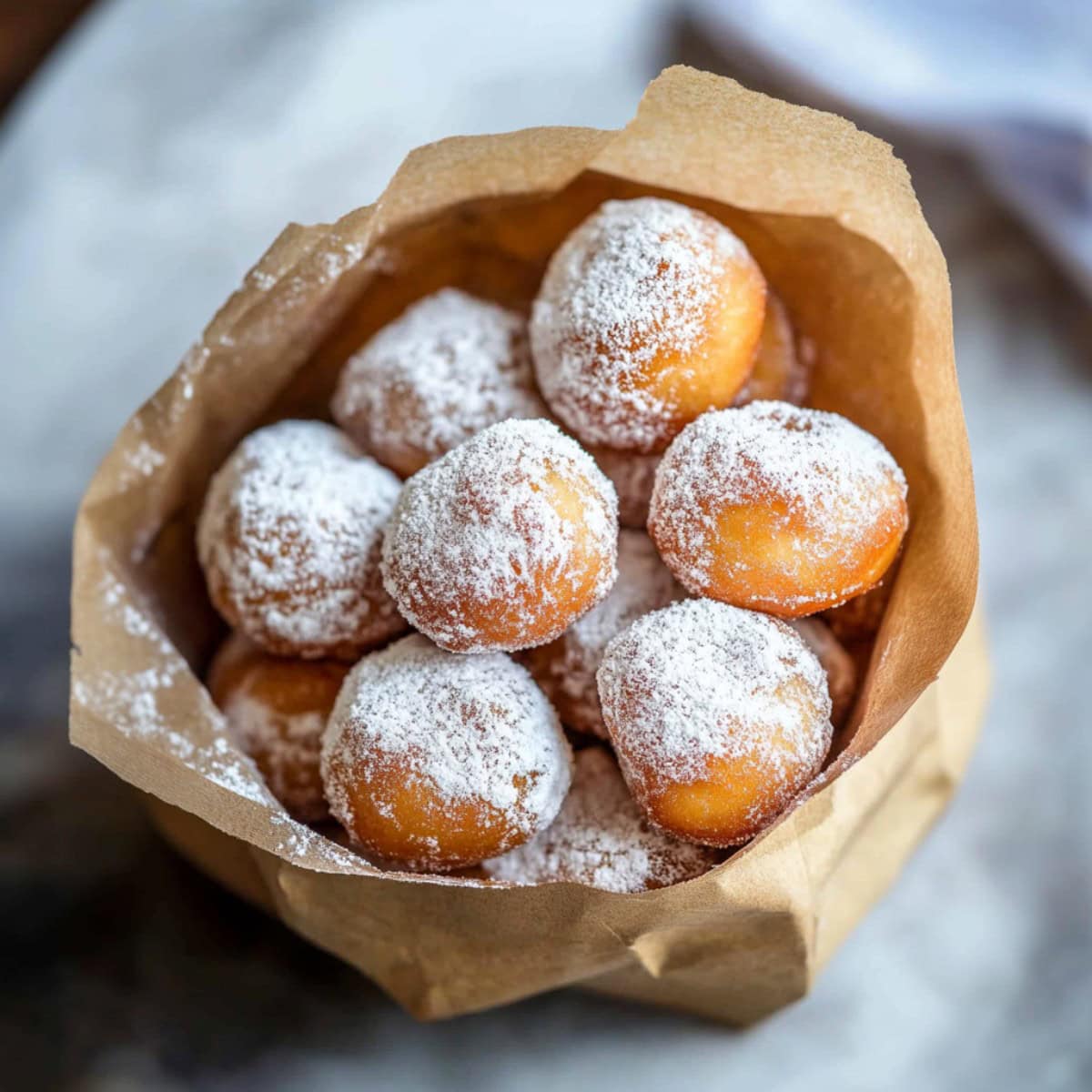 Paper bag filled with Italian donuts coated in powdered sugar.