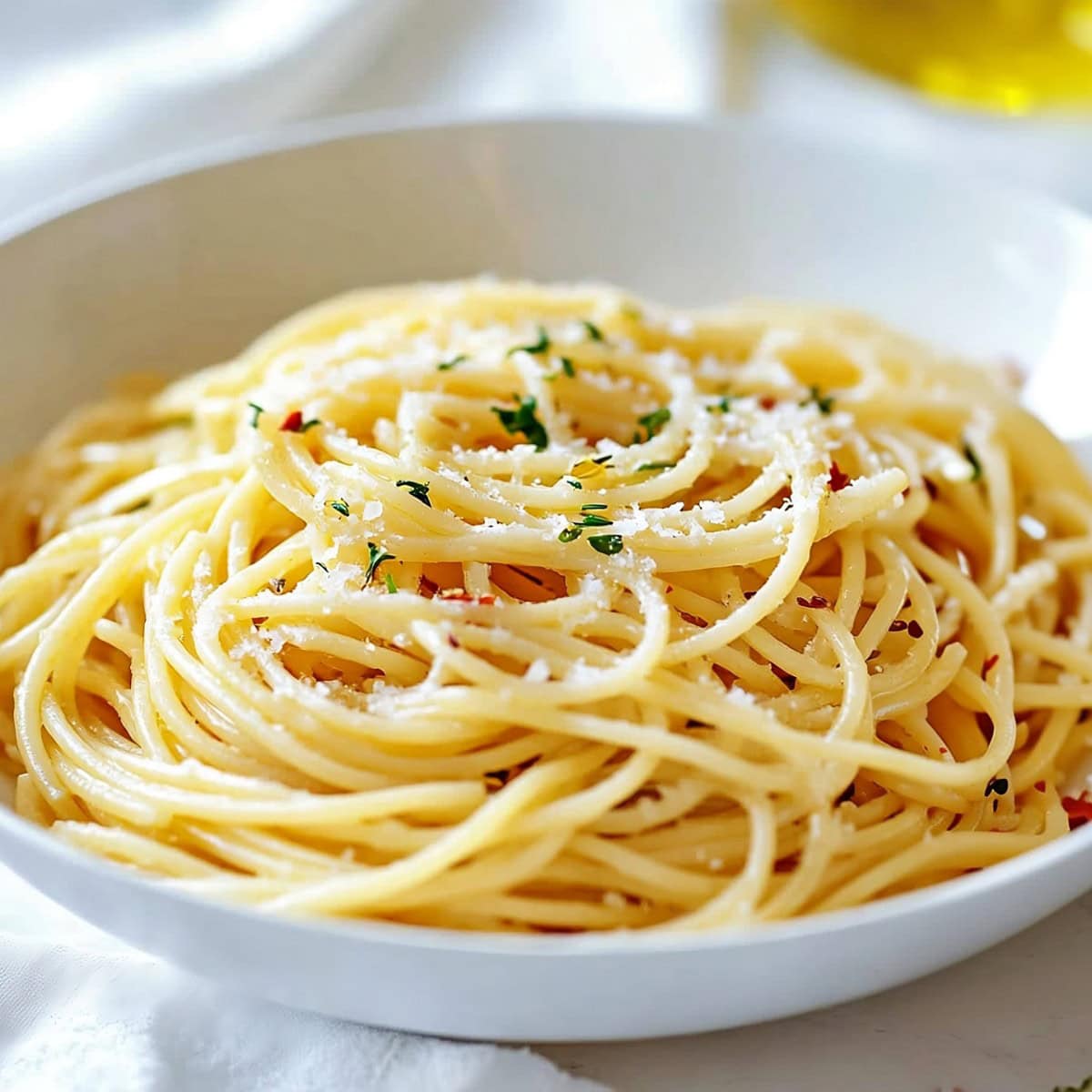 White bowl with serving of aglio e olio garnished with parmesan cheese.