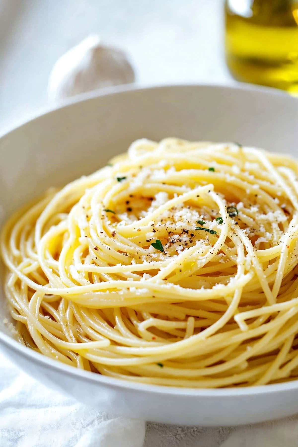 Spaghetti aglio e olio served in a white bowl garnished with parmesan cheese.