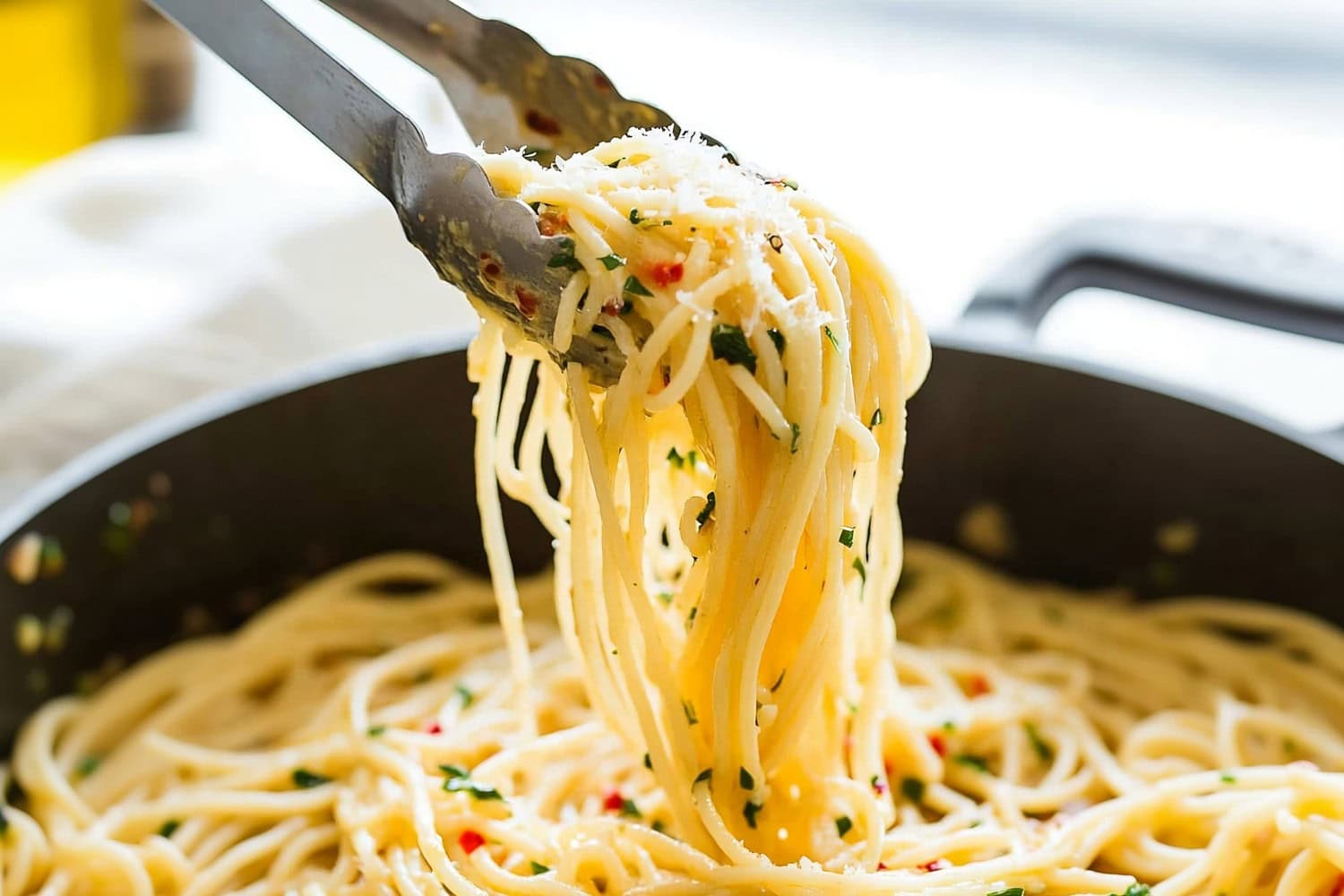 Spaghetti aglio o olio in a pan lifted with a tong.