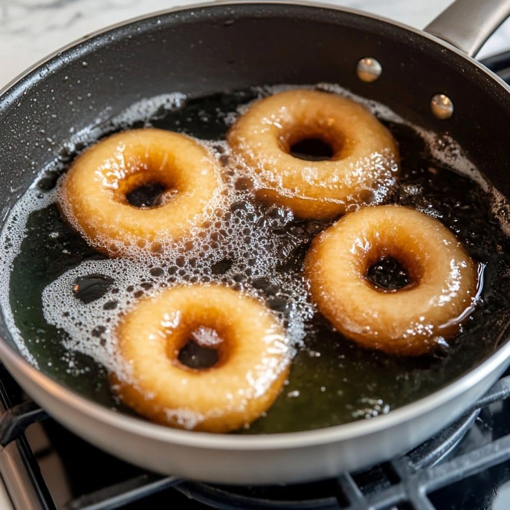 Canned biscuit donuts being deep fried in oil in a frying pan.