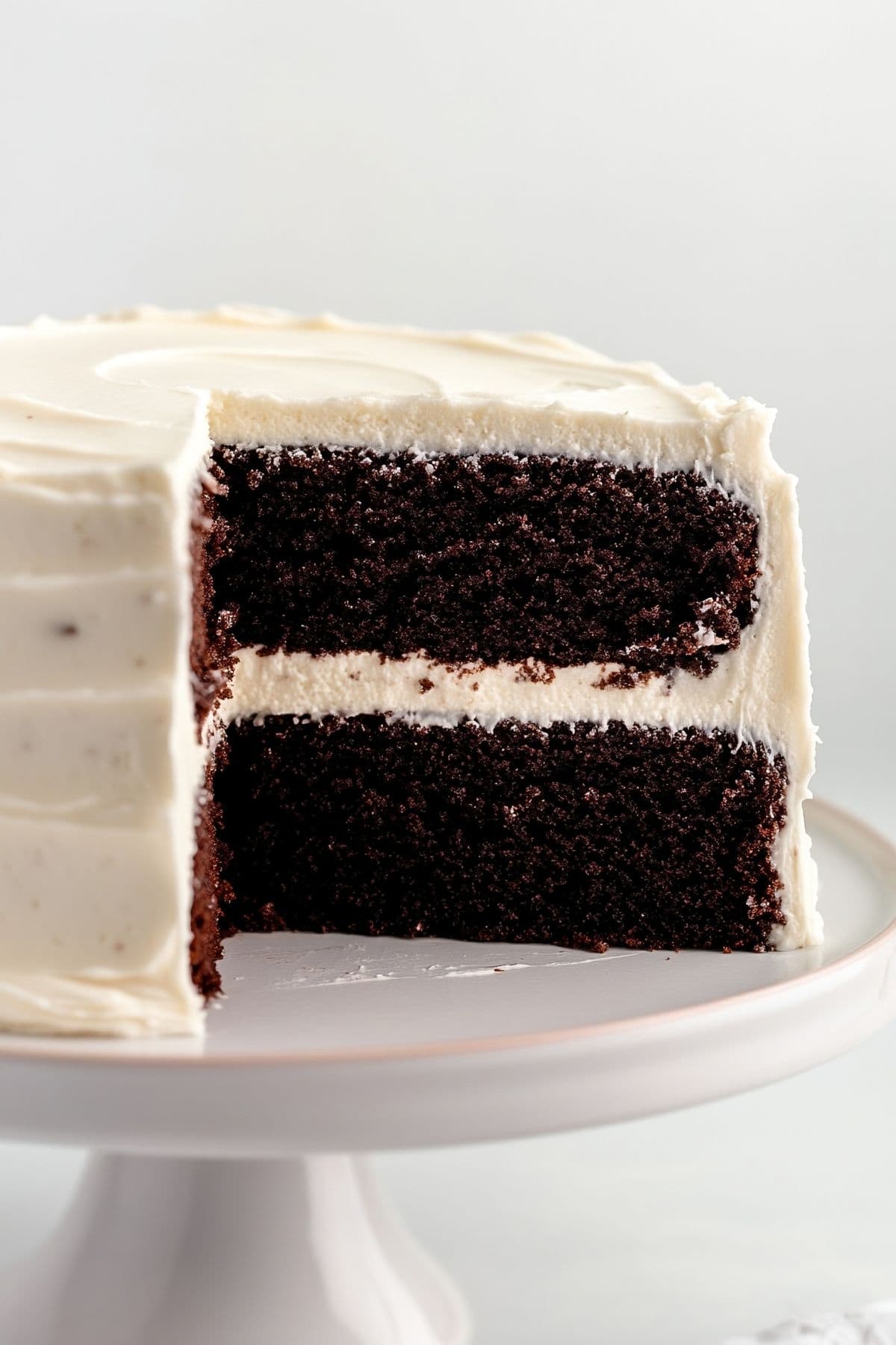 Chocolate cake with cream cheese frosting, displayed on a cake stand with a slice removed, side view