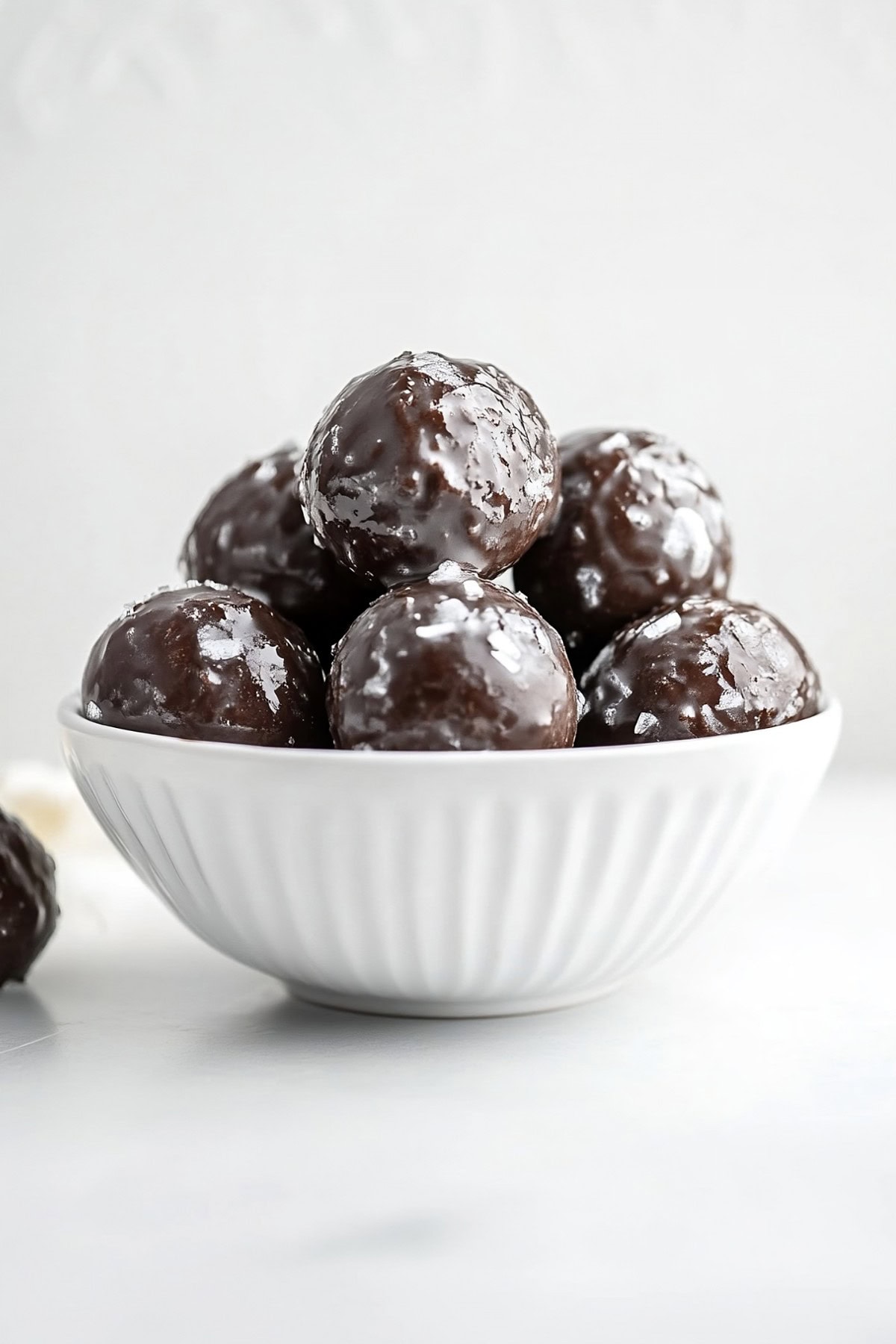 A white bowl filled with glazed chocolate donut holes, side view