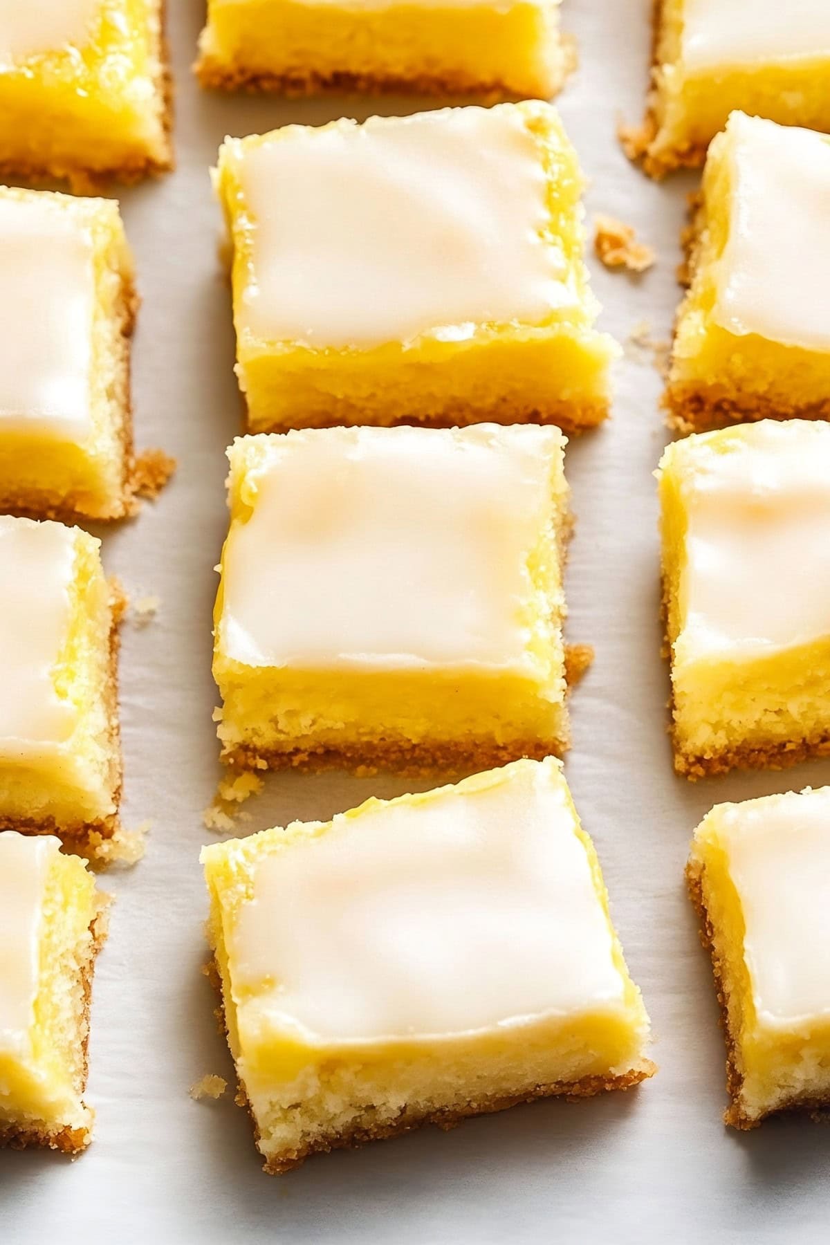 Sliced lemon brownies with lemon glaze arranged flat lay on parchment paper.