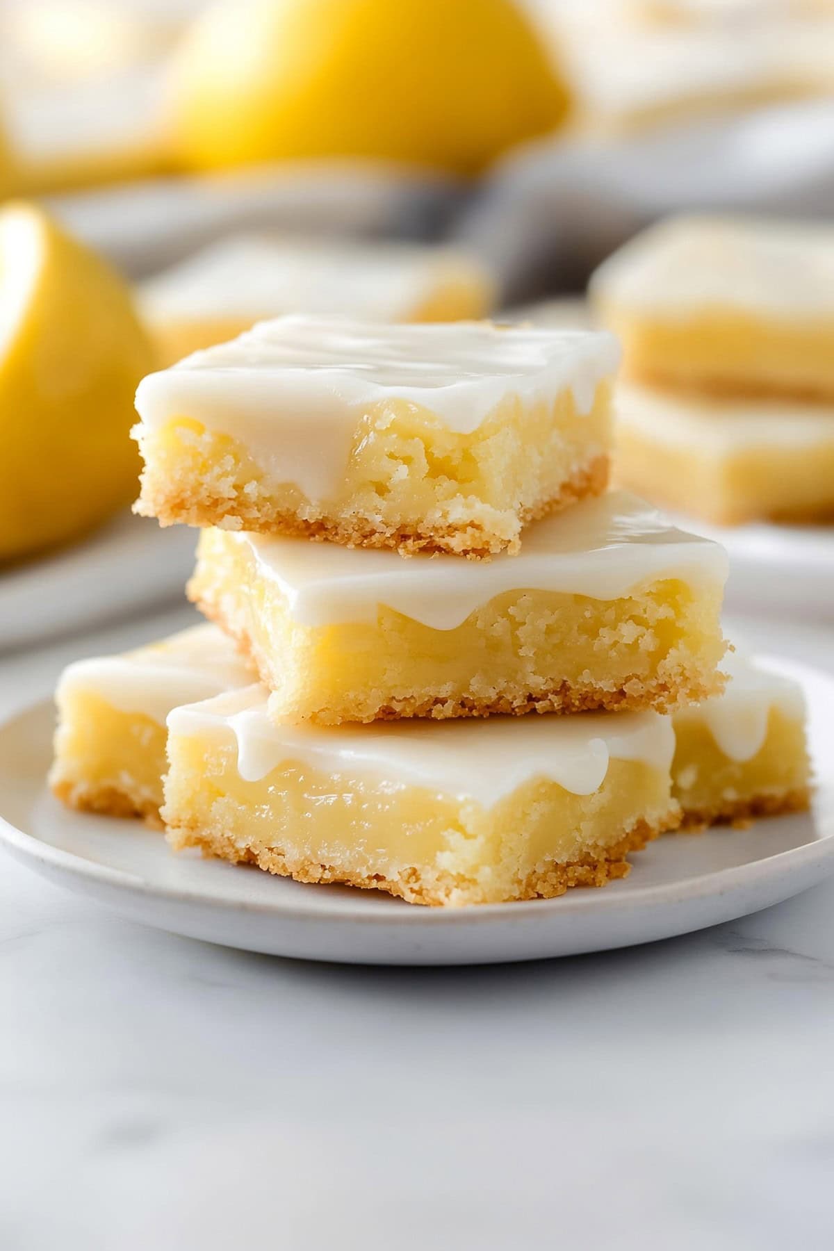 Square slices of lemon brownies stacked on top of each other on a white plate.