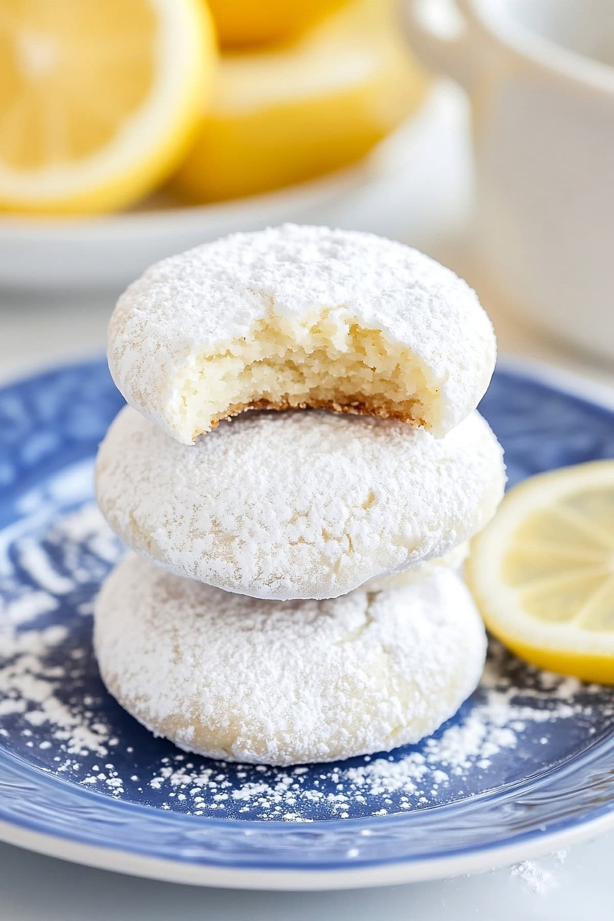 Lemon cooler cookies coated in powdered sugar stacked on top of each other served on a blue plate.