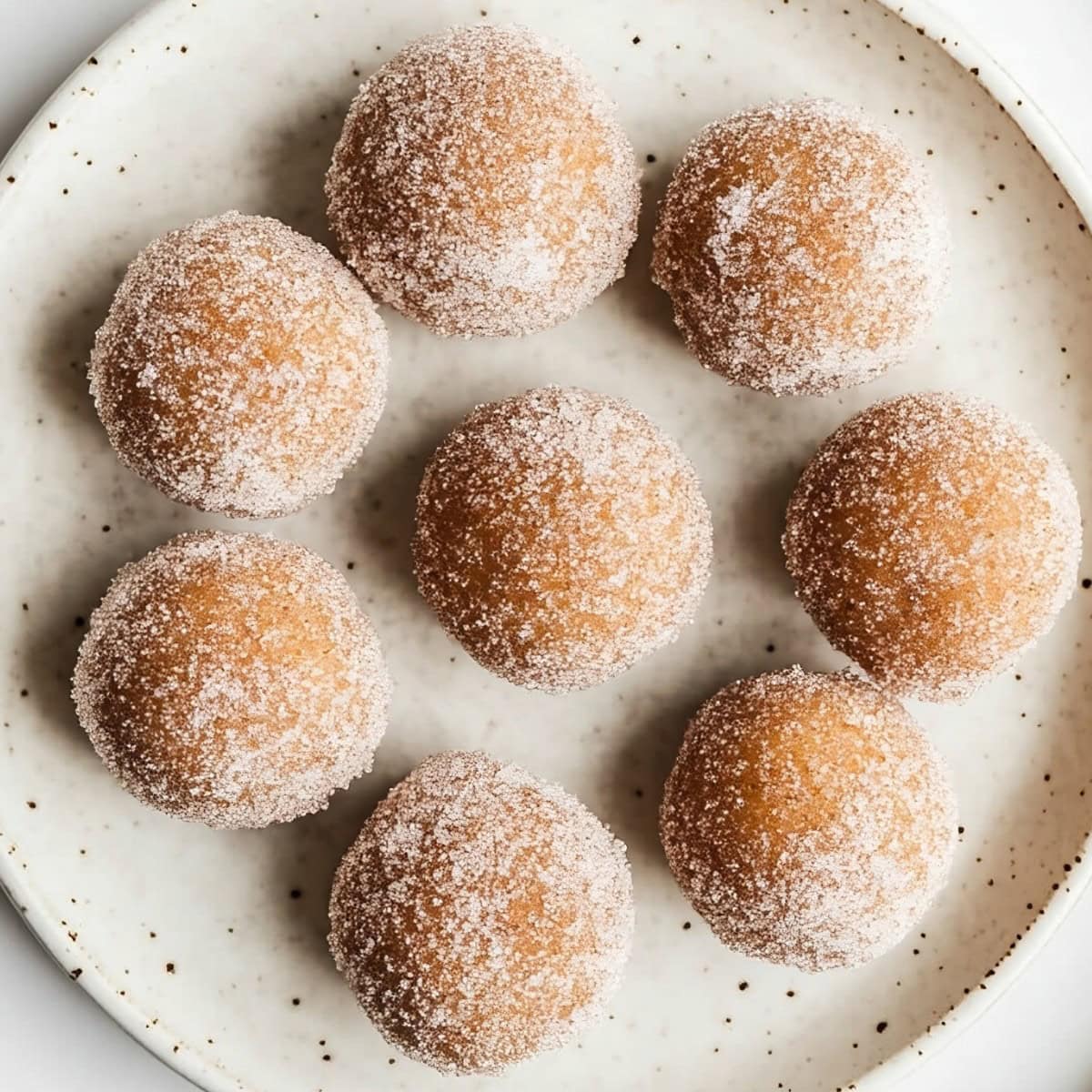 A plate of beautifully arranged baked pumpkin spice donut holes covered in sugar, top view