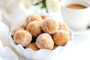 An elegant bowl filled with baked pumpkin spice donut holes, served with a cup of coffee.