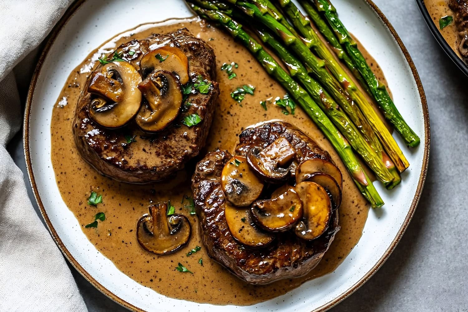 An overhead view of Steak Diane with mushrooms and asparagus on a stone table.