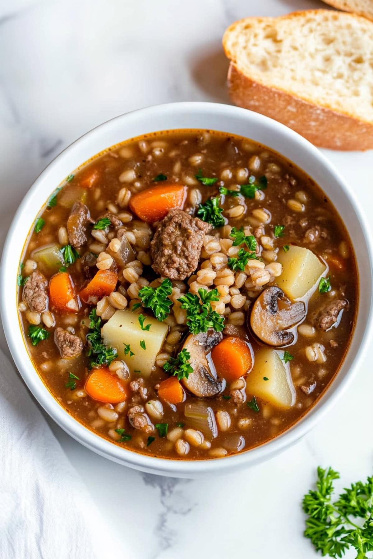 Close-up of a rich beef barley soup filled with pearl barley, diced vegetables, and flavorful broth, served in a white bowl.