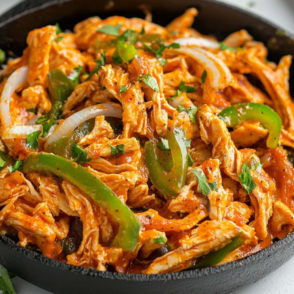 Shredded chicken with green bell peppers and onions tossed in buffalo sauce in a cast iron skillet.