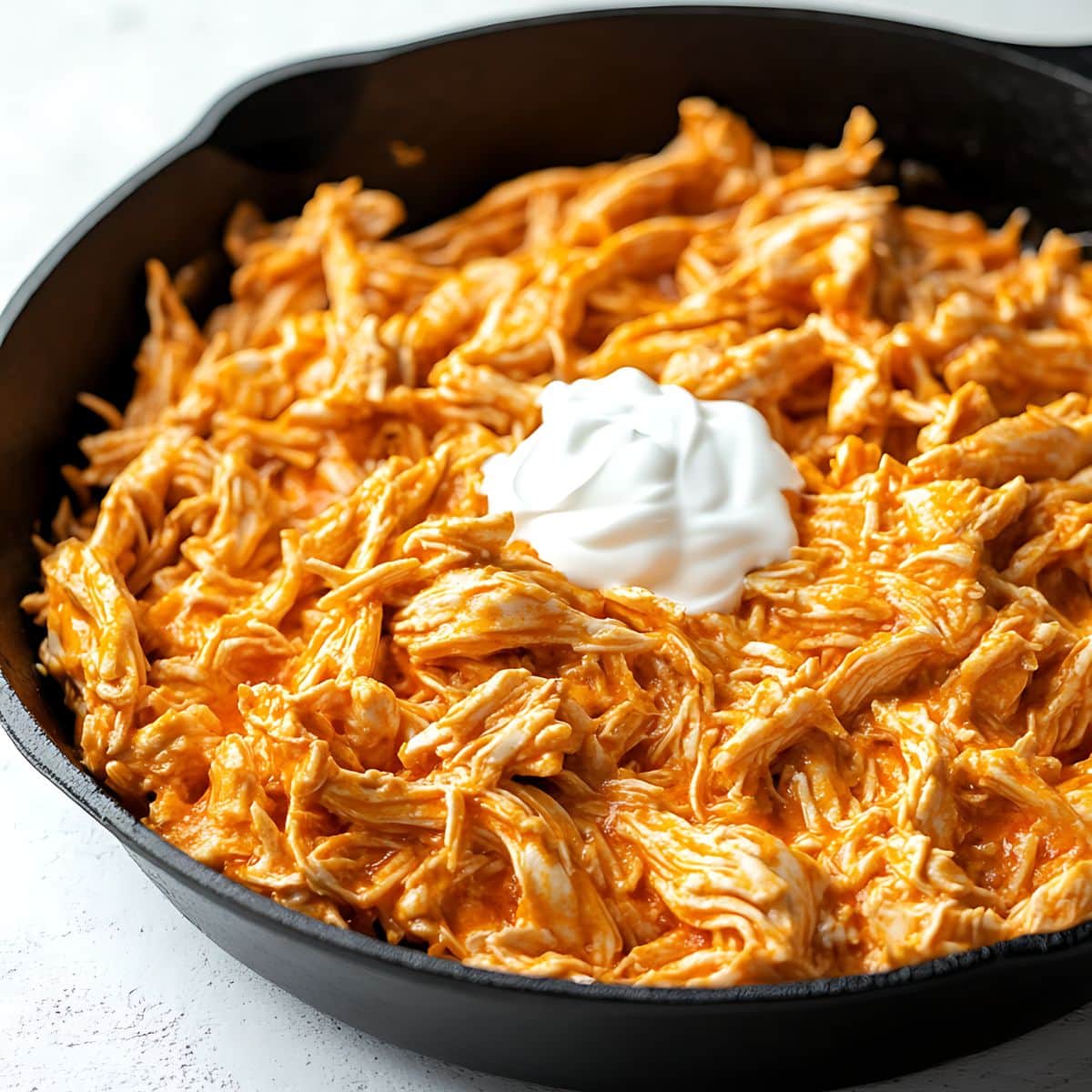 Shredded chicken with buffalo sauce in a cast iron skillet with sour cream.