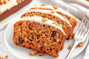 Sliced carrot cake with cream cheese frosting served in a white plate with fork.