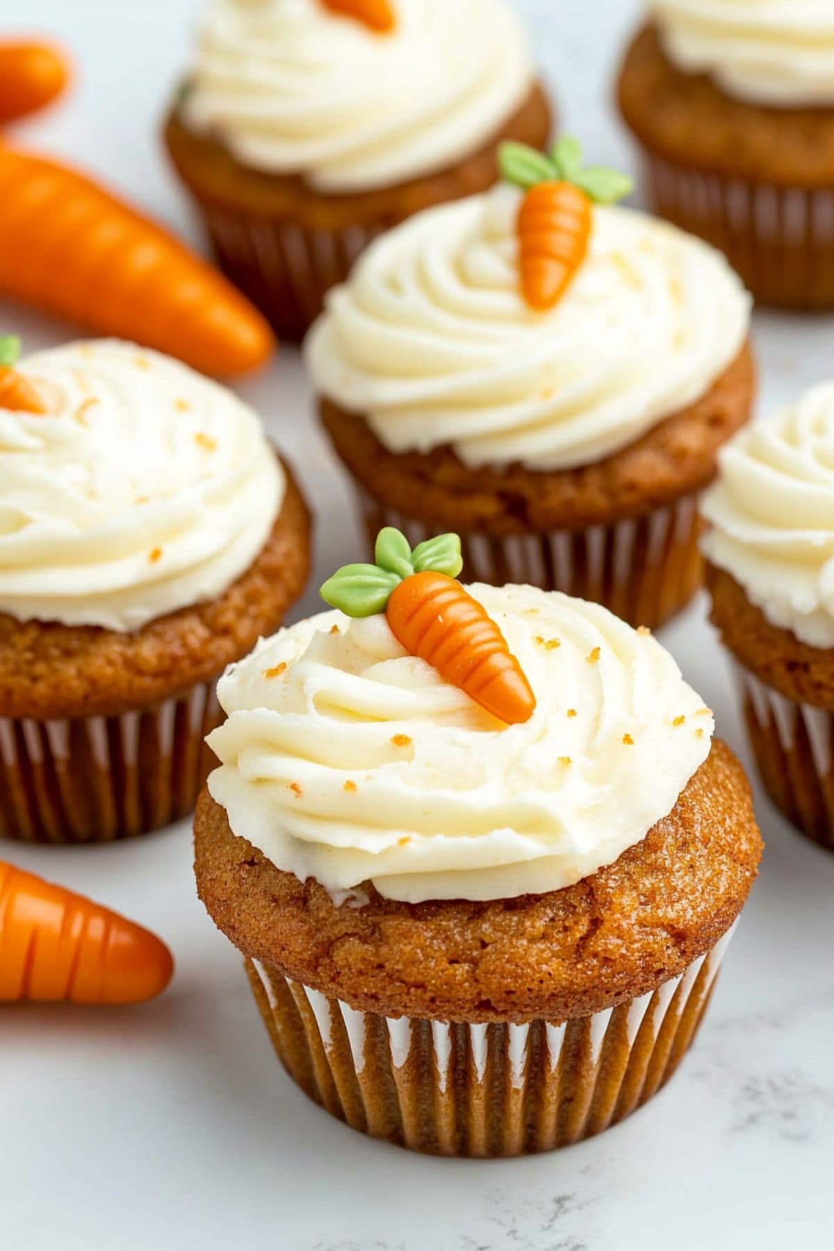 Carrot cake muffins with cream cheese frosting garnished with carrot candies on top, close up