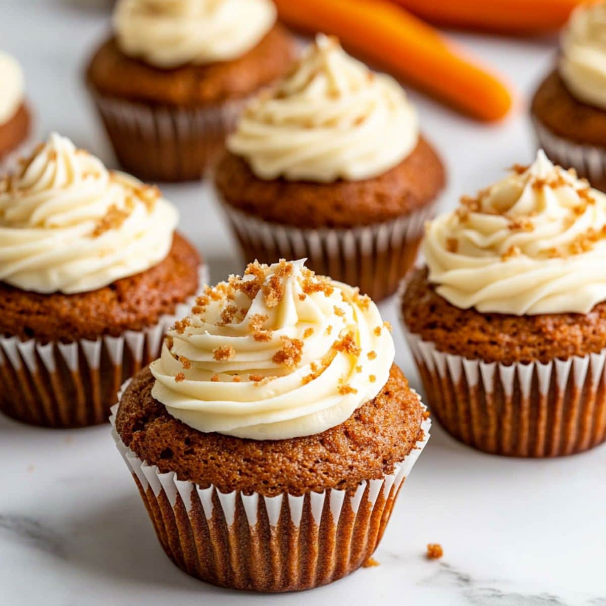 Carrot cake muffins with cream cheese frosting arranged on marble surface.